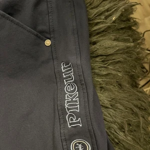 Mörkblå ridbyxor från Pikeur - Snygga mörkblå ridbyxor från Pikeur med silikongrip längs hela sätet och benen för extra grepp i sadeln. Byxorna har broderad logga på låret, klassisk femficksdesign och är tillverkade i ett stretchigt syntetmaterial som ger bra rörelsefrihet.