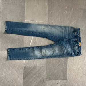 Slim Glenn blå jeans 28/30 - Snygga blå jeans från Slim Glenn i modellen slim fit. Jeansen har klassisk femficksdesign, normalhög midja och lätt slitna detaljer framtill och baktill. Perfekta för dig som gillar en smalare passform och vill ha ett par stilrena jeans i garderoben.