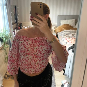 Offshoulder blommig topp i rosa och vitt - Superfin offshoulder topp med blommigt mönster i rosa och grönt på vit botten. Toppen har vida, långa ärmar och är croppad. Perfekt för vår och sommar, i ett lätt och luftigt material som känns skönt mot huden.