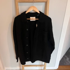 Svart stickad cardigan *Nypris: 640kr* - Svart stickad cardigan från Jack & Jones Premium. Klassisk modell med knappar framtill, bröstficka och mjuk känsla. Perfekt för lager-på-lager och enkel att styla till jeans eller chinos.