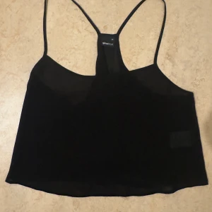 Svart transparent linnetopp Gina Tricot - Svart, tunn och transparent linnetopp från Gina Tricot med smala axelband och rak passform. Toppen har en enkel, stilren look och är tillverkad i ett lätt och luftigt syntetmaterial. Perfekt för lager-på-lager eller till ett par höga jeans.