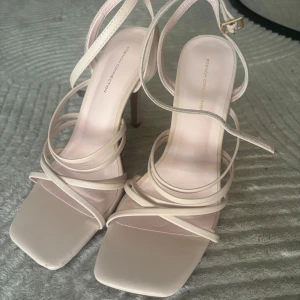 Ljusrosa sandaler från French Connection - Säljer ett par ljusrosa sandaler från French Connection med smala remmar och fyrkantig tå. Skorna har hög klack och justerbart spänne vid ankeln. Perfekta för att lyfta din outfit med en stilren och trendig vibe.