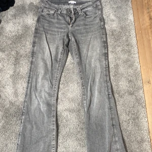 Grå bootcut jeans från Gina Tricot - Snygga grå jeans från Gina Tricot i bootcut-modell. Jeansen har klassisk femficksdesign, markerade sömmar och coola ficklock med knapp bak. Perfekta för dig som gillar en lite utsvängd look och vill ha något som sticker ut.