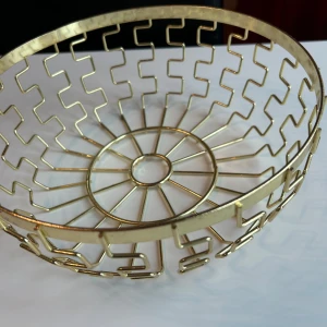 Dekorativ skål guldmetall - Bilderna visar en dekorativ skål i guldmetall med geometriskt mönster. Skålen har en modern design och är i gott skick utan synliga defekter eller slitage. Perfekt som fruktskål eller inredningsdetalj. Ingen elektronik eller teknisk funktionalitet syns.