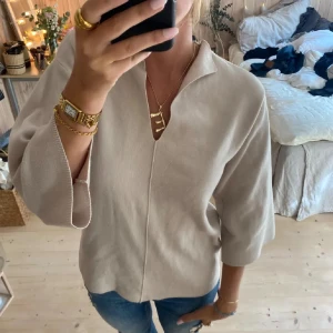 Beige tröja med krage och trekvartsärm - Stilren beige blus med krage och snygg v-ringning. Modellen har trekvartsärmar och en rak, avslappnad passform. Storlek xs men som en s