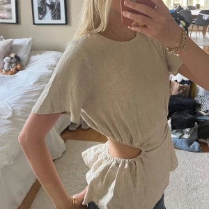 Beige linnetopp med cut out-detalj - Säljer en beige linnetopp med korta ärmar och snygg cut out i midjan. Toppen har en avslappnad passform med resår i midjan som ger en peplum-effekt 🩷🩷använd endast en gång, orginalpris 349kr, kom gärna med prisförslag 