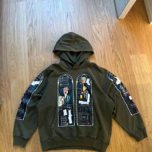 WHO DECIDES WAR x Basquiat x H&M - Olivgrön hoodie från H&M x Jean-Michel Basquiat x WHO DECIDES WAR. Basquait tryck i de klassiska WDW fönsterna på bröstet och ärmarna. Stor skön luva, ribbade muddar och en loose passform. Materialet är mjuk bomullsmix, perfekt för dig som gillar streetwear med unik design. Aldrig använd