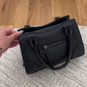 Svart handväska med dragkedja - Säljer nu min svarta trendiga/eftertraktade väska från Ginatricot i fint skick, men några snören/trådar har lossnat men inget jag tycker man tänker på kanske går att limma ihop, därav priset