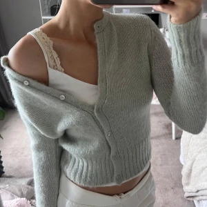 Ljus- grå/grön/turkos stickad kofta från Zara - Supermjuk och mysig ljusgrå stickad kofta från Zara. Modellen är croppad med rund halsringning och knappar framtill. Perfekt att slänga över ett linne eller t-shirt. Långa ärmar och ribbade muddar ger en snygg och enkel look. Använd fåtal gång så den är i bra skick. Koftan är i storlek S men skulle säga att den upplevs lite mindre i storleken, den är mer som en S/XS. Förövrigt är den också bekväm att ha på sig.