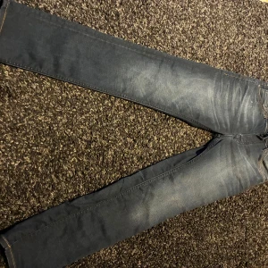 Mörkblå Jack and Jones  jeans W27 L30 - Säljer ett par mörkblå Jack and Jones jeans med klassisk femficksdesign och snygga slitningar framtill. Jeansen har smal passform och raka ben, med detaljerade sömmar och läderpatch bak i midjan. Perfekta för dig som gillar stilrena och moderna jeans.