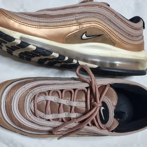 Nike Air Max 97 i roséguld - Säljer ett par Nike Air Max 97 sneakers i snygg roséguld och beige med ikoniska vågiga linjer och synlig luftbubbla i sulan. Skorna har snörning och svart detalj på insidan. Perfekta för dig som vill sticka ut med stilrena och trendiga sneakers.