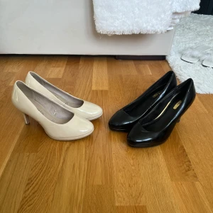 Beiga och svarta pumps med klack - Två par klassiska pumps, ett par i blankt beige och ett par i blankt svart. Båda har rund tå och smal klack, det svarta paret är lite slitna. Materialet är syntet med glansig finish. Storlek 37. Säljs tillsammans för 140 kr