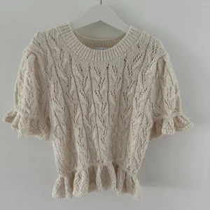 Beige stickad topp med volang från Zara - Supersöt beige stickad topp från Zara med korta ärmar och volangdetaljer vid ärmslut och nederkant. Använd några grå gånger men i nytt skick💕Säljer den då den är för liten. Nypris 299