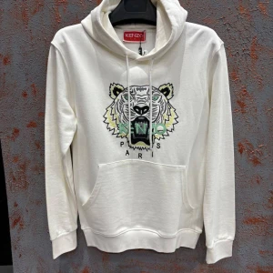 Vit Kenzo hoodie med tigerbrodyr - Säljer en vit hoodie från Kenzo med ikonisk tigerbrodyr och Kenzo Paris-text framtill. Tröjan har huva med snörning, magficka och långa ärmar. Perfekt för dig som vill sticka ut med en streetstyle-look.