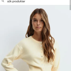 Ljusgul kofta med pärlemorknappar - Supersöt ljusgul kofta med rund halsringning och pärlemorskimrande knappar framtill. Tröjan har lång ärm och är ribbad vid ärmslut och nederkant. Perfekt för lager-på-lager och ger en fräsch look till din outfit.