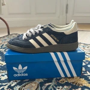 Adidas Spezial sneakers i mörkblå mocka - Säljer ett par Adidas Spezial sneakers i mörkblå mocka med creme vita detaljer. De blå snörena medföljer i köpet. Skorna har använts dagligen men har inga större skador. Skriv vid funderingar!!