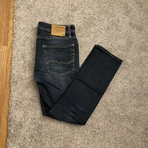 Jack & Jones jeans - Snygga mörkblå jeans från Jack & Jones Originals med klassisk femficksdesign och kontrastsömmar på bakfickorna. Jeansen har rak passform och är tillverkade i slitstarkt denimtyg med lätt tvättade detaljer för en cool look. Stl 32/30