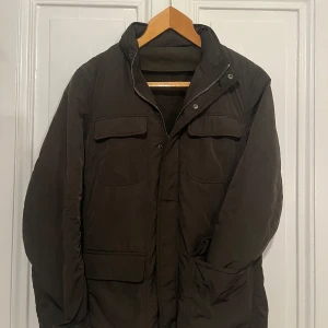Mörkgrön feildjacket - Säljer en mörkgrön feildbacket från Massimo dutti som går att vända ut och in och göra till kavaj. Kavajen har klassisk krage, tre knappar framtill och fickor. Feildjackan är quiltad och ger extra värme. Perfekt för dig som vill ha en stilren look med en twist.