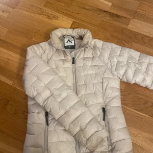 Beige pufferjacka från McKinley - Snygg beige pufferjacka från McKinley i storlek 36. Jackan har quiltad design, hög krage och dragkedja framtill samt två dragkedjeförsedda fickor. Perfekt för kyliga dagar och enkel att matcha med olika outfits.