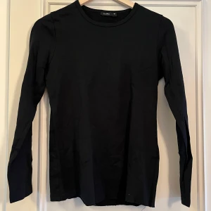 Svart långärmad tröja från Lindex - En basic svart långärmad tröja från Lindex i mjuk bomull. Tröjan har rund halsringning och en rak passform som funkar till allt. Perfekt att styla lager på lager eller bara som den är.