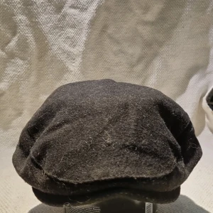 Svart ullkeps från Celtic Ore Tweed - Snygg svart keps i klassisk flat cap-stil från Celtic Ore Tweed. Tillverkad i en blandning av ny ull och har ett quiltat foder på insidan för extra komfort. Perfekt accessoar för dig som gillar tidlös och stilren look.