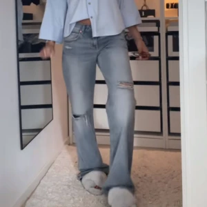 Ljusblå slitna jeans - Ljusblå jeans från Zara med raka ben och slitningar på knäna. Klassisk femficksmodell med låg midja och knappgylf. Perfekta för en avslappnad och trendig look.