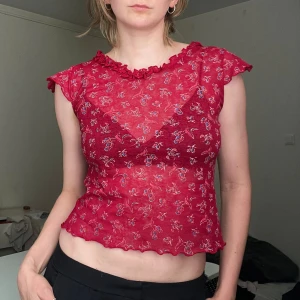 Röd blommig mesh topp med volang - Säljer en röd 2000s mesh topp med små blommor i blått och vitt. Toppen har volangkant vid halsringningen. Ingen lapp men gissar att strl är 36ish. Jag på bilden är 170cm och har strl 36 på överdelar, använd köp nu <<33