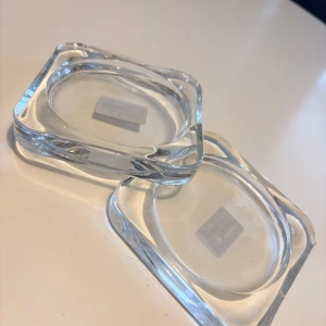 Ljusunderlägg - Två glasunderlägg. De är tillverkade av klart glas och har en modern, stilren design. Passar utmärkt som dekorativa tillbehör i hemmet.