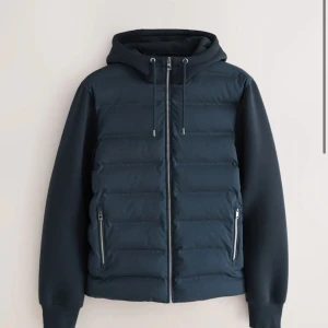 Next hybrid jacka - Snygg mörkblå pufferjacka med huva och dragkedja framtill. Jackan har quiltad front, släta ärmar och två fickor med dragkedja. Perfekt för kyliga dagar. Såldes ut snabbt. 