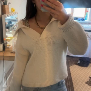 Vit stickad tröja med krage - Säljer en vit stickad tröja med v-ringning och bred krage. Tröjan har lång ärm och en avslappnad passform, perfekt att styla med jeans eller kjol. Ribbstickade muddar vid ärmslut och nederkant ger en snygg detalj. Storlek S Gina Tricot. Knappt använd💞Postar inom 1-2 dagar! Skriv för frågor