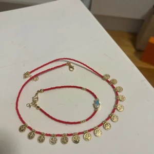 Rött halsband och armband med guldberlocker - Set med halsband och armband i röda pärlor, dekorerade med små runda guldberlocker. Armbandet har även en blå evil eye-detalj. Snyggt och trendigt smyckeset som ger färg och glans till din look. En kurdisk traditionell sett 