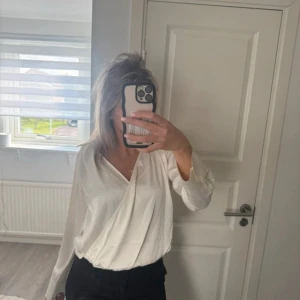 Vit omlottblus från H&M, stl S - Säljer en fräsch vit omlottblus från H&M i storlek S. Blusen har lång ärm, v-ringad omlottfront och är tillverkad i ett mjukt, lätt material som ger en clean och stilren look. Perfekt att matcha med svarta jeans eller kjol för en snygg outfit.