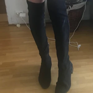 Svarta overknee stövlar med klack - Säljer ett par svarta overknee stövlar med låg klack och rund tå. Stövlarna har dragkedja på insidan och är gjorda i mockaliknande material. Perfekta för att lyfta vilken outfit som helst med sin höga och stilrena look.