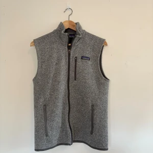 Grå fleeceväst från Patagonia - Grå fleeceväst från Patagonia. Västen har tre fickor med dragkedja och en stilren, enkel design. Perfekt för lager-på-lager och outdoor-vibes.