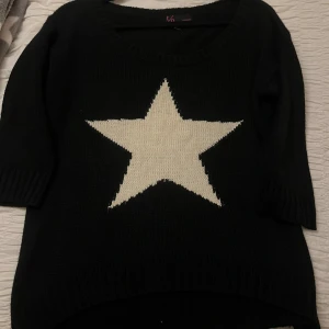 Svart stickad tröja med stjärna t/o - Svart stickad tröja från t/o med stor vit stjärna framtill. Tröjan har rund halsringning, ribbade muddar och en något längre bakdel. Perfekt för dig som vill ha en cool och mysig look med lite edge. Tre kvarts ärm