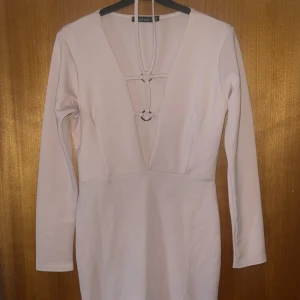 Rosa kortklänning från Boohoo - Säljer en rosa kortklänning från Boohoo med lång ärm och snygg djup v-ringning med snörningsdetaljer framtill. Klänningen har en figurnära passform.