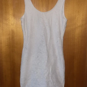 Vit spetsklänning från Gina Tricot - Supersöt vit kortklänning från Gina Tricot med spetsdetaljer och ärmlös design. Klänningen har en snygg v-ringning i ryggen och figurnära passform.