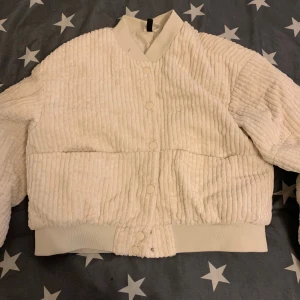 Vit teddyjacka från H&M Divided S - Supermjuk och fluffig teddyjacka i storlek S. Jackan är vit med breda ribbade detaljer, knäppning med tryckknappar och ribbade muddar vid ärmslut och midja. Perfekt för dig som gillar en cozy och trendig look.