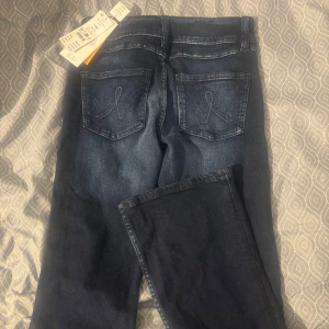 Mörkblå jeans med bootcut - Snygga mörkblå jeans från Ginatricot med bootcut och dubbla knappar i midjan. Jeansen har klassiska bakfickor med broderad detalj och är tillverkade i stretchigt denim för skön passform. Perfekta för dig som gillar en tidlös look med lite extra edge.