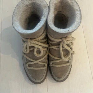 Inuikii classic beige - Säljer ett par beige boots från Inuikii med grova snören och mjuk, fluffig insida. Skorna har mocka och skinn på utsidan, samt mörkbrun sula. Perfekta för kalla dagar. Skon har ett mindre hål (se bild) men går att laga av någon händig. 