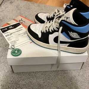 Nike Air Jordan 1 Mid University Blue - Nike Air Jordan 1 Mid University Blue med svart, vit och ljusblå färg. Klassisk high-top siluett i skinn med snörning och ikoniska Jordan Wings-loggan på sidan. Snygg blå yttersula och svart swoosh. Pris går att diskutera.