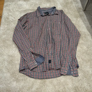 Rutig skjorta från Bondelid XL - Riktigt snygg rutig skjorta från Bondelid i storlek XL. Skjortan har blå, röda och vita rutor, klassisk krage och långa ärmar med kontrasttyg på insidan av manschetterna. Perfekt för dig som gillar en avslappnad men stilren look.