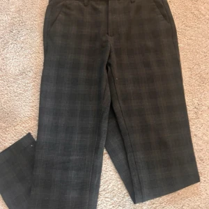 Rutmönstrade kostymbyxor Jack & Jones - Mörkgrå kostymbyxor från Jack & Jones med diskret rutmönster. Klassisk rak passform med hällor för bälte och sidfickor. Perfekta för en clean och stilren look. Materialet känns mjukt och har en snygg struktur.