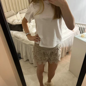 Beige virkade shorts med spetsdetaljer - Säljer ett par superfina beige shorts med virkade spetsdetaljer och snyggt mönster. De har en loose passform och är perfekta för sommaren. Shortsen har en unik och bohemisk vibe som verkligen sticker ut.