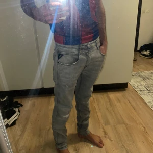 Replay grå slim jeans herr - Säljer ett par gråa Replay jeans i slim fit med slitna detaljer på benen. Klassisk femficksmodell med dragkedjegylf och snygga sömmar. Jeansen har en modern look och är tillverkade i mjukt denimtyg för skön passform.