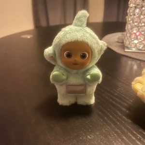 Teletubbies Vinyl Series Figurine - Söt Teletubbies-figur från POP MART Vinyl Series, tillverkad i mjuk plysch och plast. Mintgrön färg med holografisk detalj på magen. Produkten är i mycket gott skick, den har bara stått på min bokhylla. Perfekt för samlare eller som present.