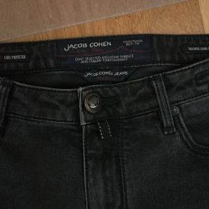 Svarta jeans från Jacob Cohën, stl 33 - Svarta jeans från Jacob Cohën i klassisk femficksmodell. Snygga detaljer och exklusiv känsla, tillverkade i ett mjukt bomullstyg med stretch. Perfekta för dig som gillar stilrena svarta jeans.