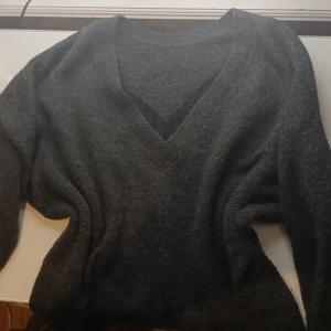 Mörkgrå stickad tröja med spets från ONLY - Mysig mörkgrå stickad tröja med v-ringning och svart spetsdetalj längs halsringningen. Tröjan har långa ärmar och en klassisk, avslappnad passform. Perfekt för lager-på-lager och chill höst- eller vinterstil.