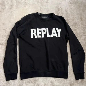Svart sweatshirt från Replay - Svart sweatshirt från Replay med stor vit logga framtill. Klassisk rund halsringning och långa ärmar. Tillverkad i mjuk bomull för en skön och avslappnad stil. Perfekt för dig som gillar streetwear och enkel design.