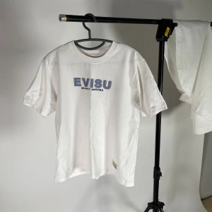 Vit Evisu t-shirt med blå tryck - Vit t-shirt från Evisu med blått 'EVISU MIGHTY DARUMA'-tryck på bröstet. Extremt bra kvalité och är i princip i nyskick. Köpt på farfetch finns kvitto. nypris 1190. 